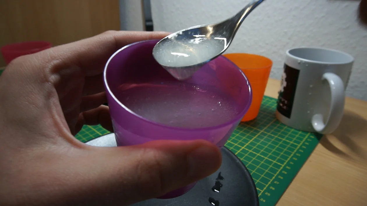 Xanthan gum mixture in a cup, running of a spoon. Note the more opaque color and the tendency of the gelatinous consistency to form pieces.