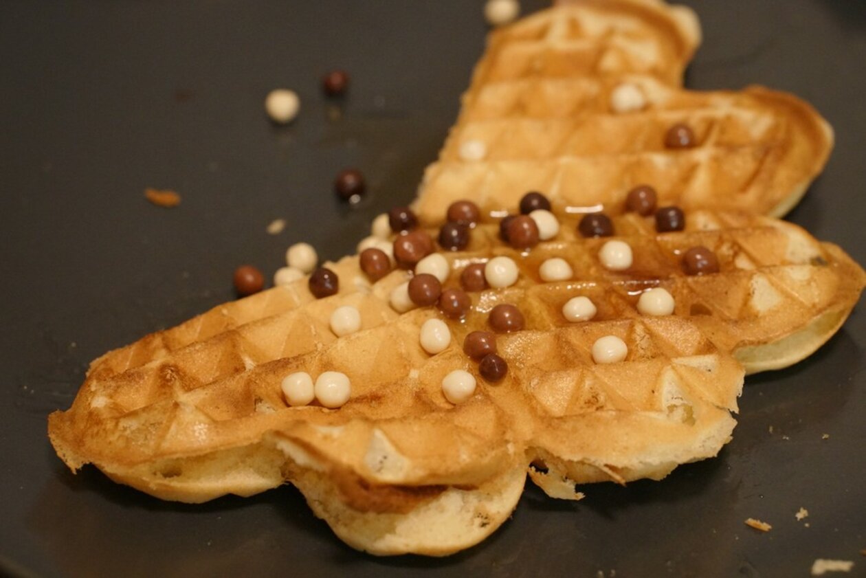 About half a crispy golden
waffle with small chocolate balls on it on a black plate.